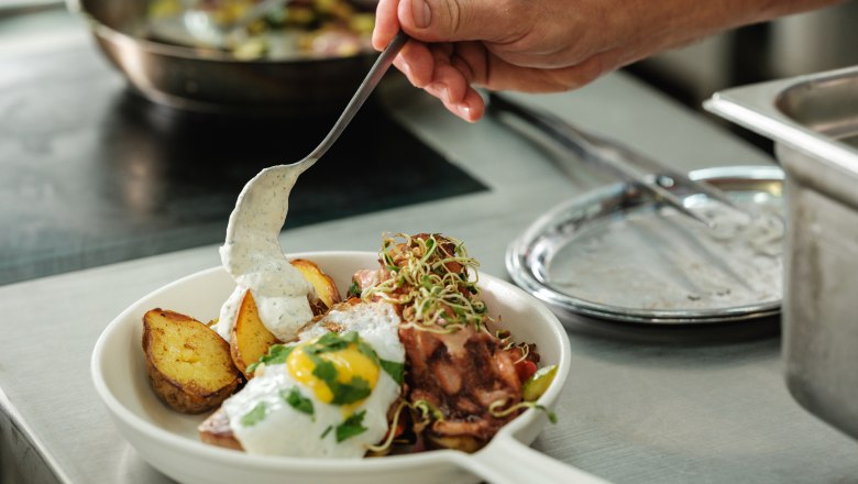 Ein Teller mit gebratenen Kartoffeln, Spiegelei und Sauce wird in einer Küche angerichtet.