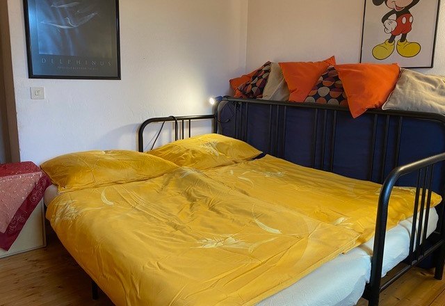 Dům na hřišti, © Helen Brugat Ložnice se žlutým ložním prádlem, plakáty na stěně a polštáři na posteli.