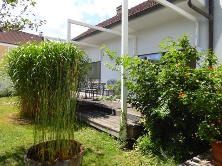 Terrasse mit Pflanzen und Gartenm&ouml;beln vor einem wei&szlig;en Haus.