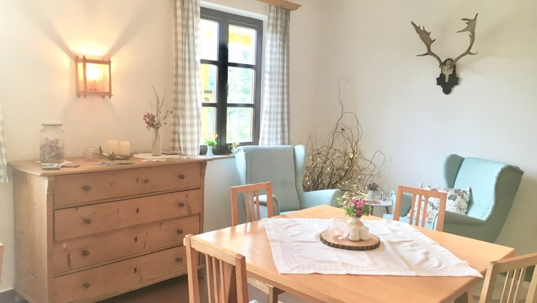 Gemütlicher Frühstücksraum mit Holztisch, Stühlen, Kommode und Dekorationen.