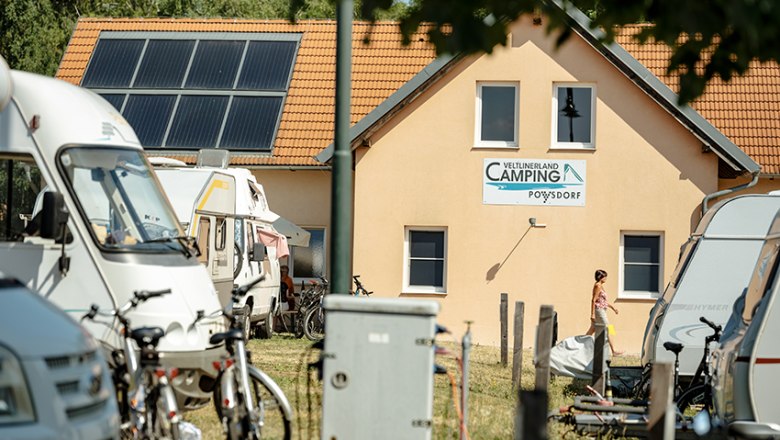 Campingplatz mit Wohnmobilen und Sanit&auml;rgeb&auml;ude im Hintergrund.